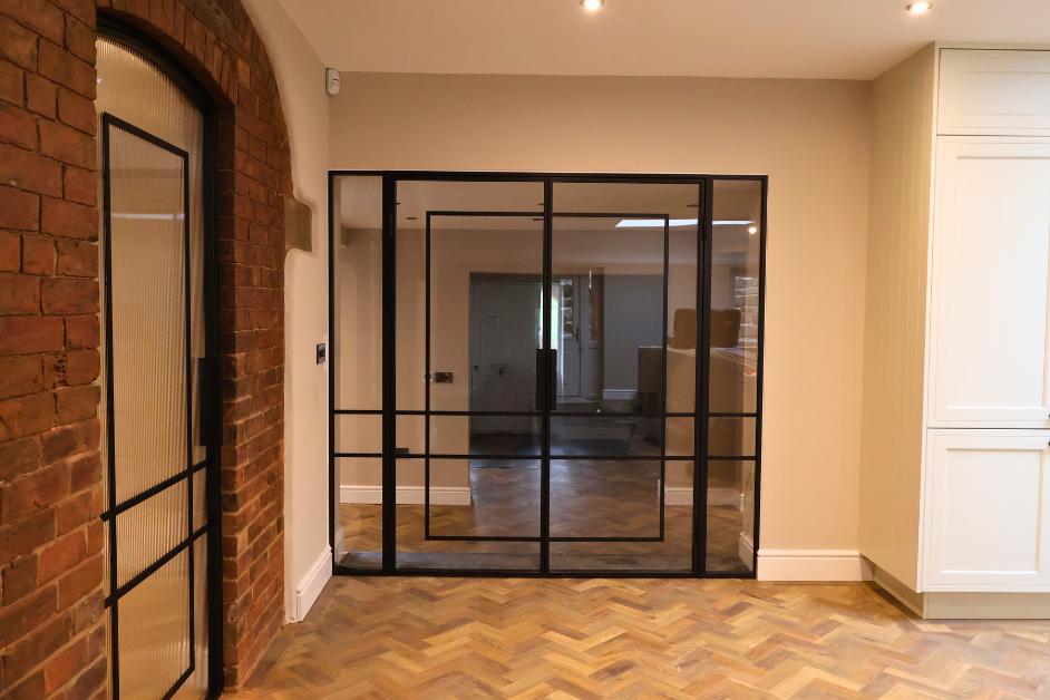 Double steel doors with fixed side panels connecting an open plan kitchen and hallway, allowing natural light to flow throughout the space.