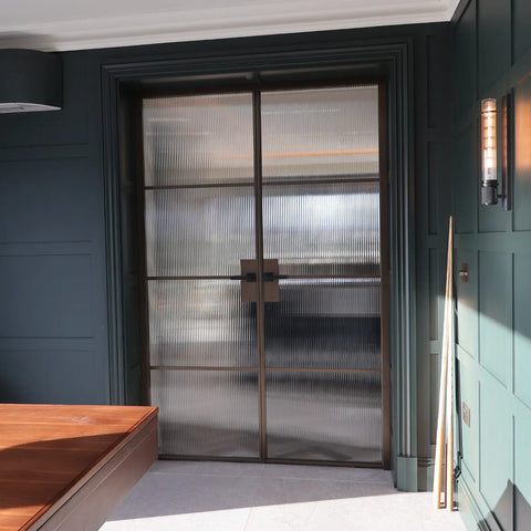 A pair of double glass doors with fluted glass and a dark bronze metal frame, set within a dark green paneled interior.