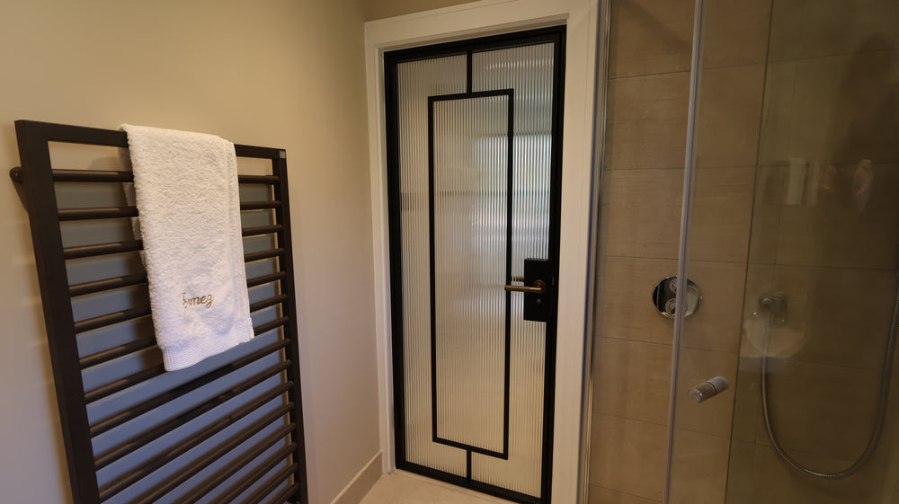 Black steel framed bathroom door with fluted glass and slim sightlines in a contemporary Surrey bathroom. Internal steel door with Deco gunmetal handle.