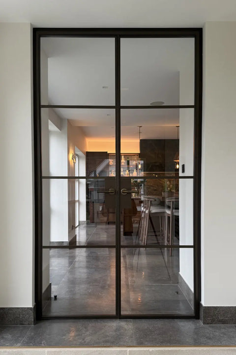 Manor House Bronze steel door, installed in a modern interior entryway with a view of a kitchen and dining area in the background.