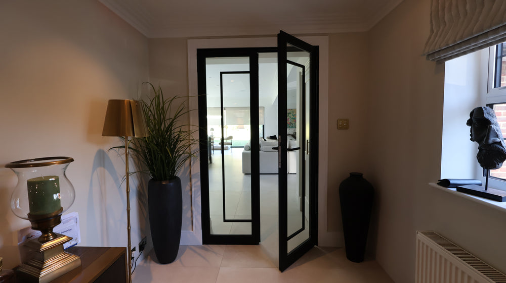 Black fire-rated steel double doors with slim sightlines connecting hallway and kitchen spaces