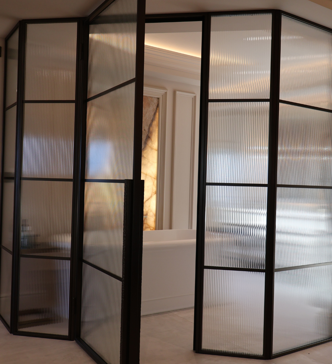 Black steel door with fluted glass and fixed side panels separating an en suite, providing privacy whilst allowing natural light to flow through the interior.
