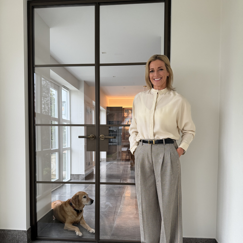 Gabby Logan standing in a modern interior setting with a dog by a glass door.