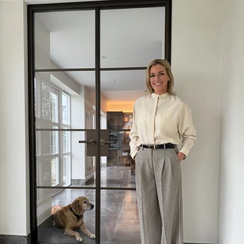 Gabby Logan stud next to her Steel Doors, with a dog lying on the floor inside the room. The doorway has a black Manor House Bronze frame and glass panels.