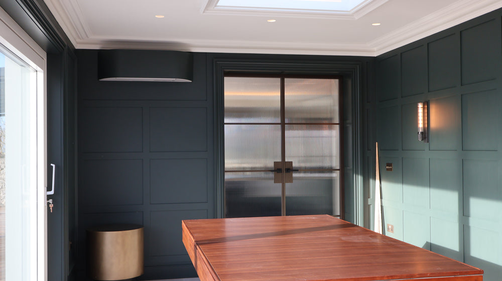 Modern interior with a fluted steel door and wooden table against a dark paneled wall in Anglesey