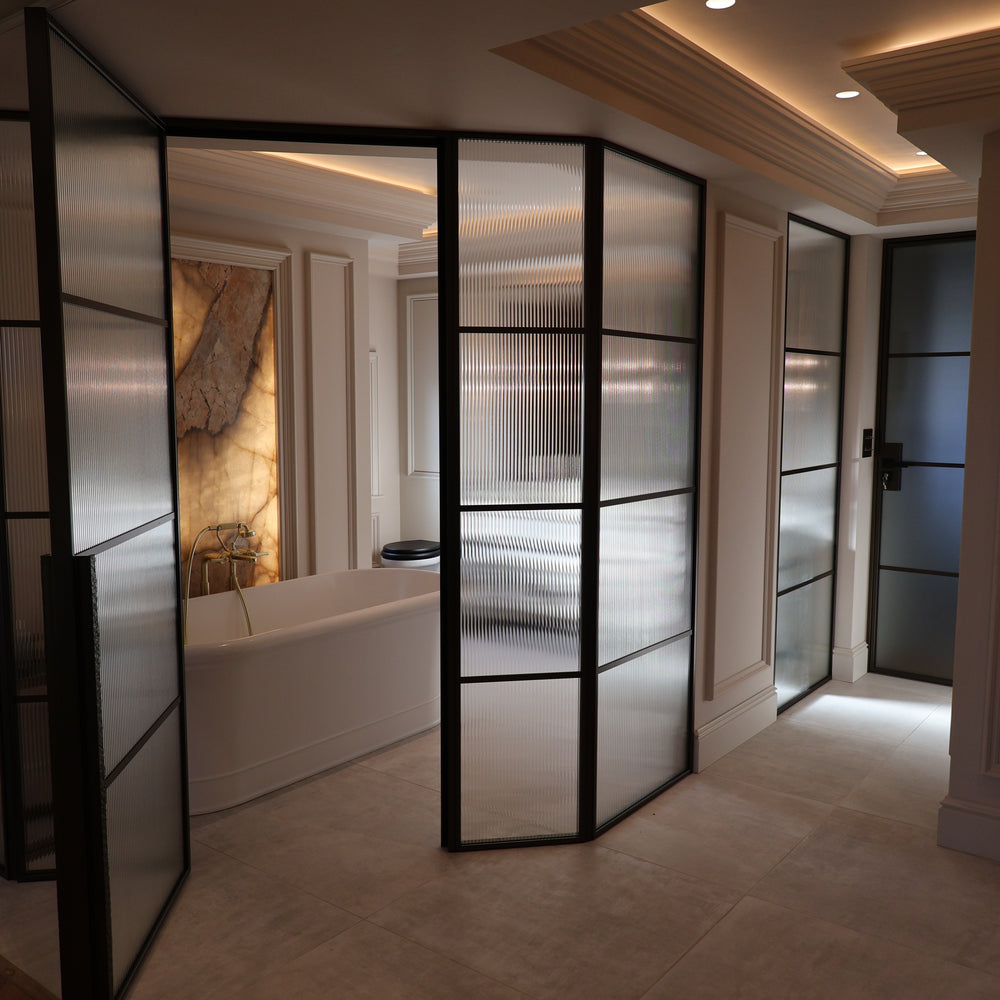 Single steel door with fixed side panels and fluted glass leading to an en suite in an Anglesey home, offering privacy whilst allowing natural light through.