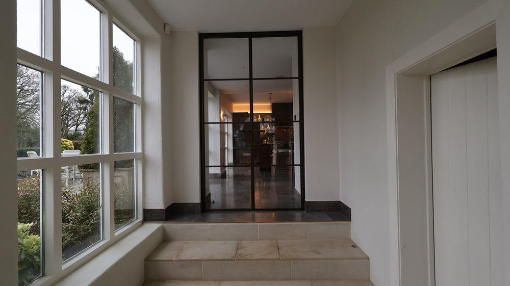 Bronze double steel doors in the Manor House style connecting the kitchen and hallway in a contemporary interior.