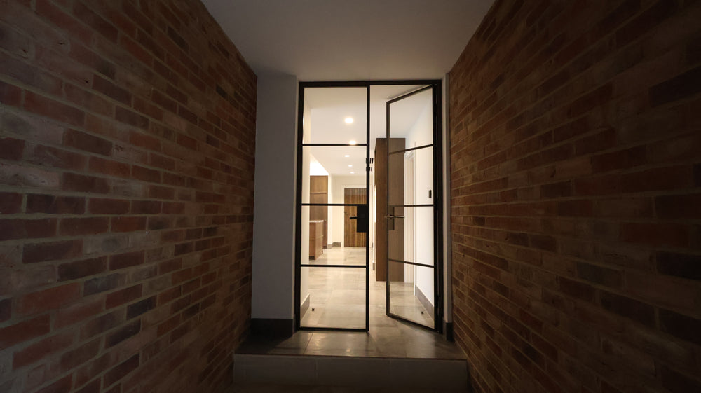 Narrow hallway with brick walls with a Manor House Bronze double steel door