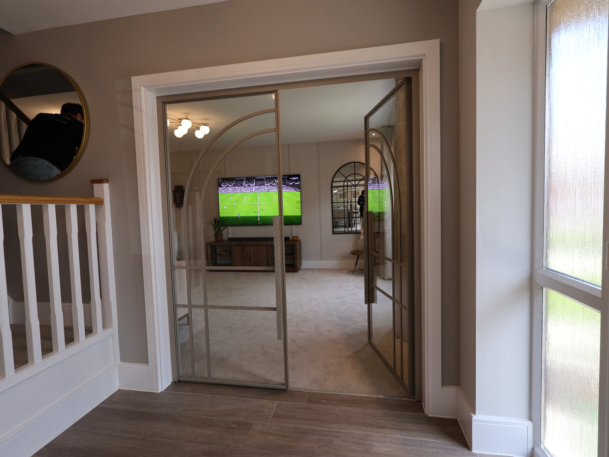 Hallway with glass doors leading to a room with a TV displaying a sports event.