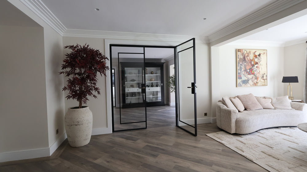 Black steel double doors with slim sightlines dividing open-plan living spaces in a contemporary Surrey home. Internal steel framed doors allowing natural light to flow through the interior.
