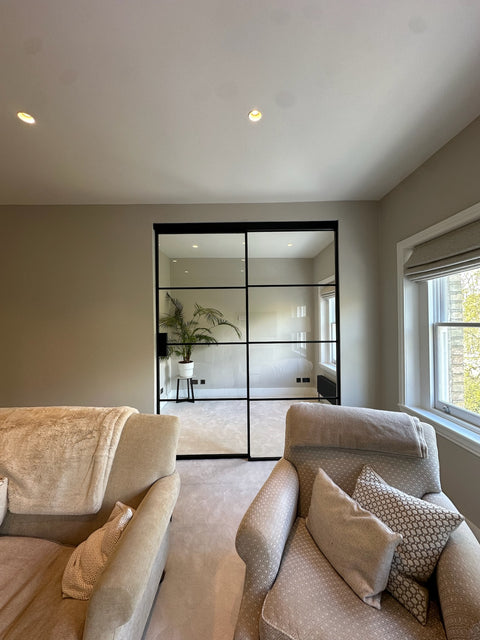 Modern living room with beige sofa, decorative pillows, and a glass door leading to another room.