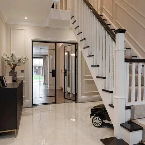 Modern interior entryway with a white staircase featuring black steps and handrails, black-framed glass doors, glossy white tile flooring, and a dark console table on the left.