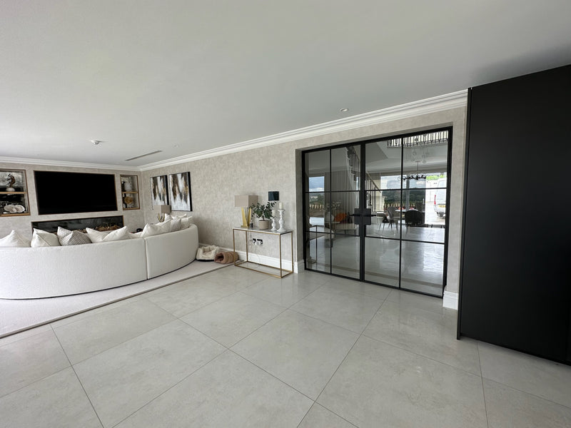 Modern living room with a large flat-screen TV, white sofa, and glass door.