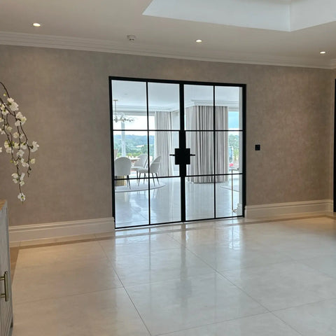 Black metal frame steel doors installed in a modern room with beige textured walls and light-colored tiled floors.