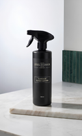 Black spray bottle labeled on a marble surface with a neutral background