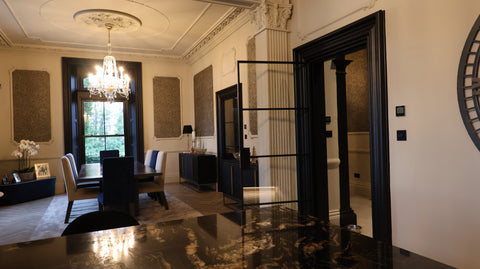 Dining room with a chandelier, chairs, and a large open steel door leading to another room.