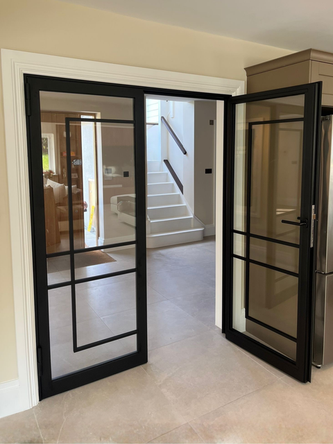 Steel fire door with slim black steel sightlines and glass panels separating corridor and kitchen