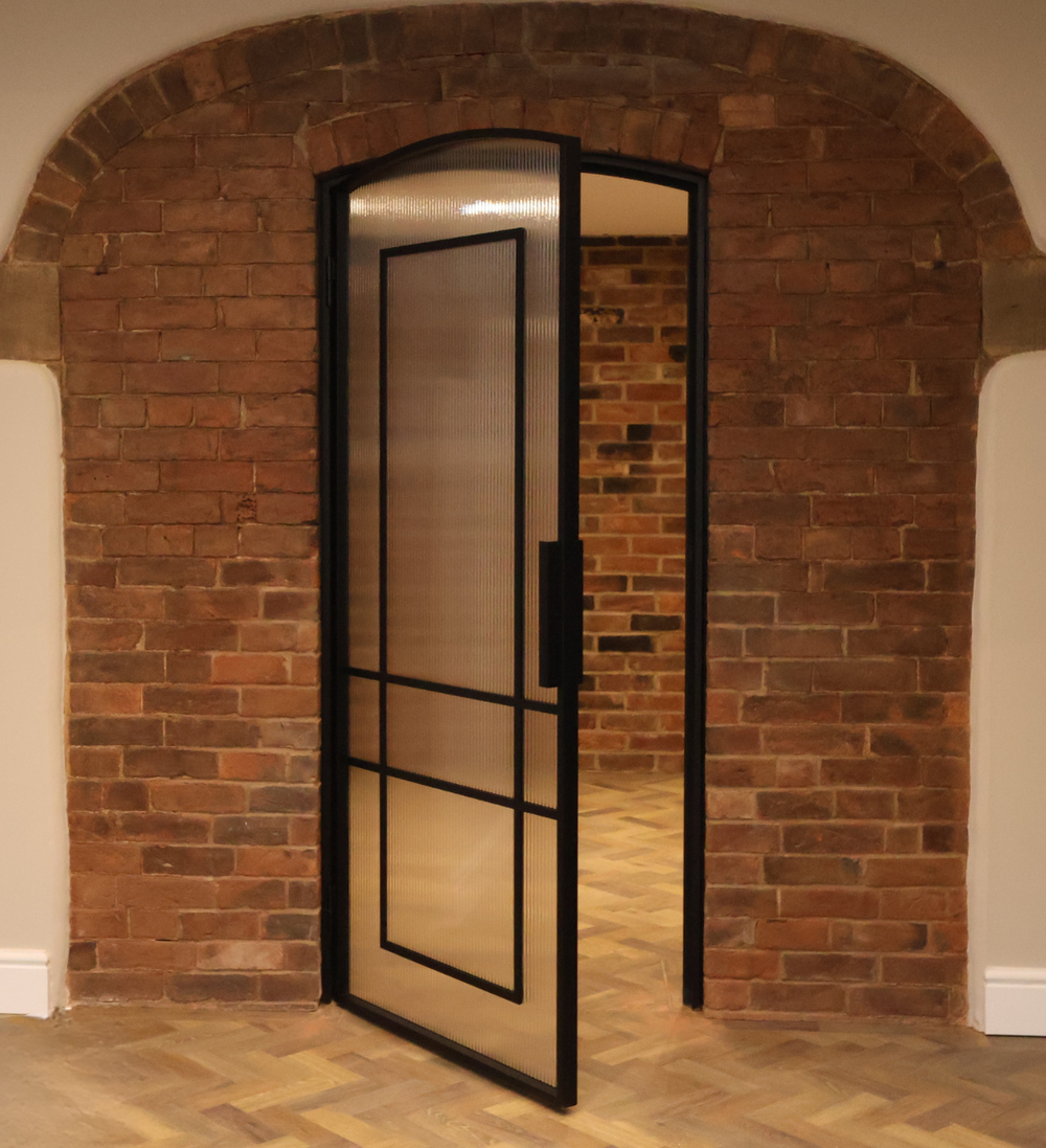 Steel and fluted glass door with black frame in a brick wall setting